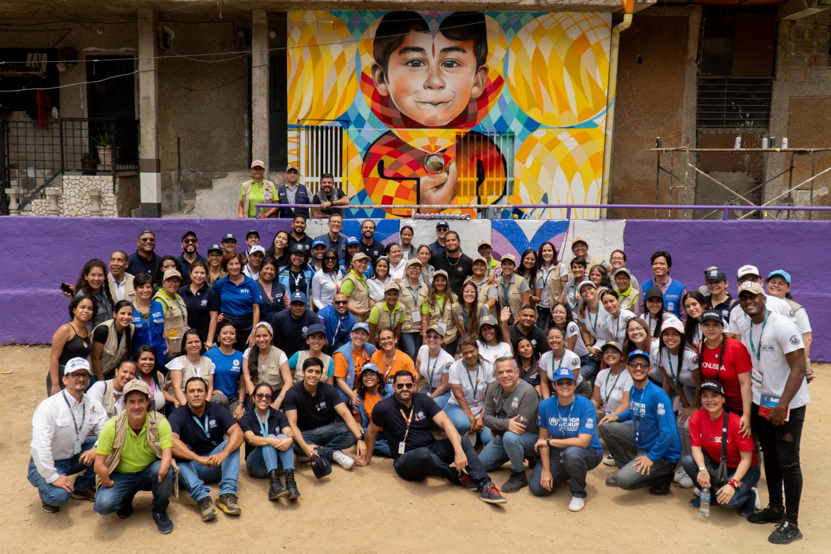 Un grupo de personas sonríe a la cámara frente a un mural.
