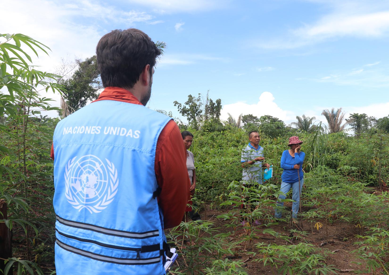 Personal de OCHA con un chaleco de Naciones Unidas observa a una familia de campesinos.