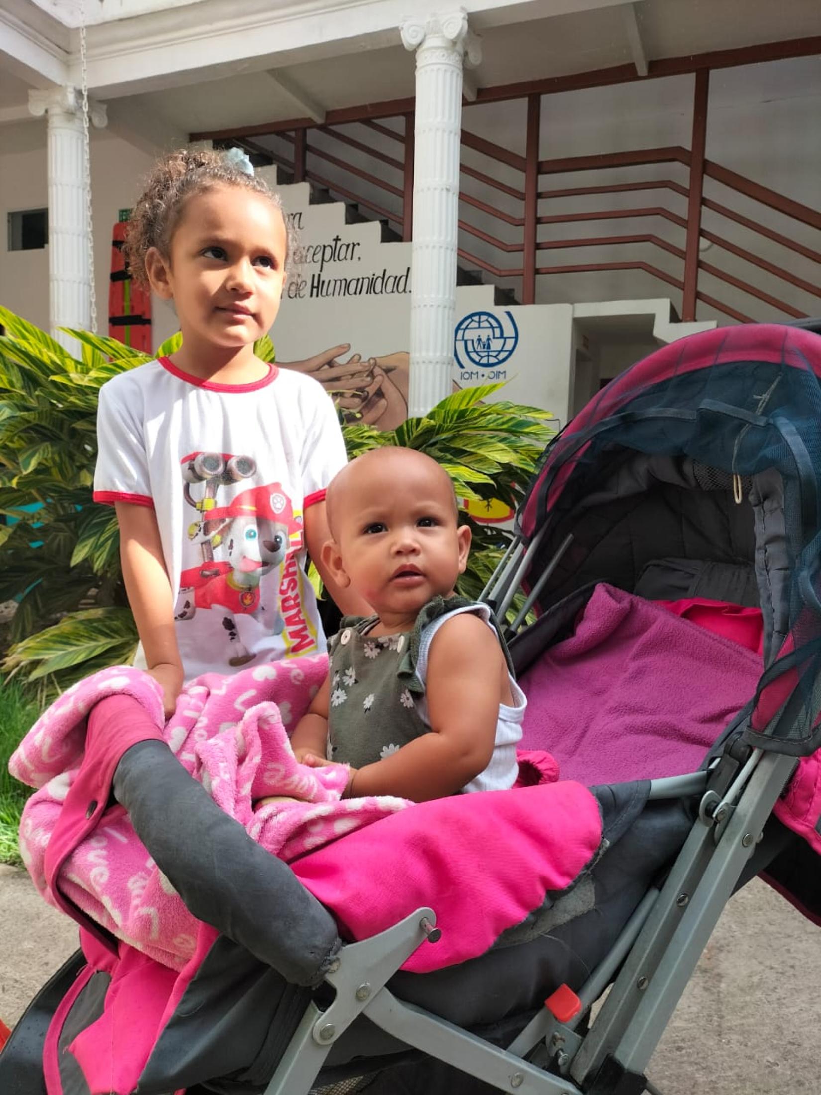 Un bebe y una niña miran a la cámara.
