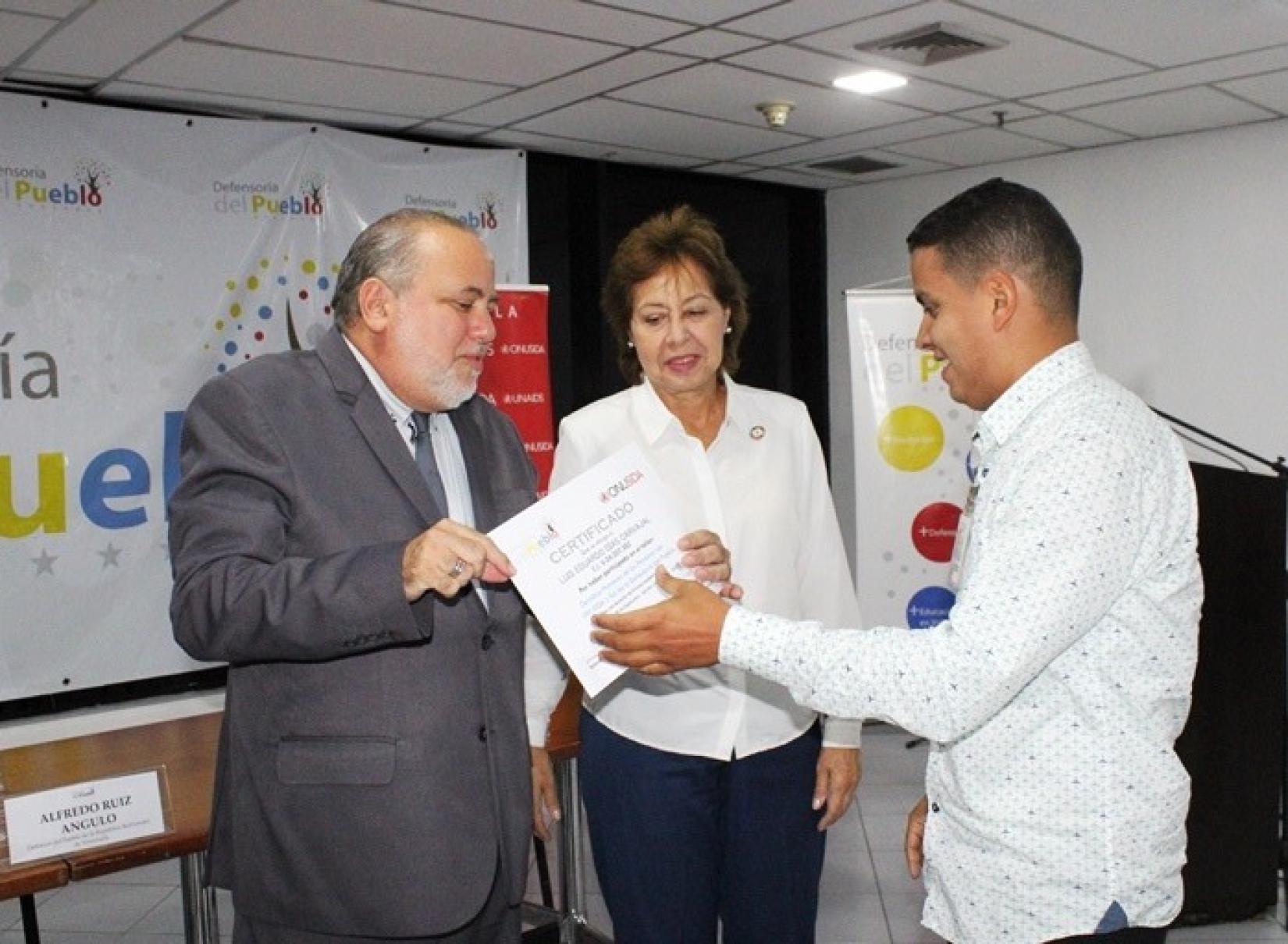 La Directora de País de ONUSIDA y el Defensor del Pueblo entregan un certificado a un participante.