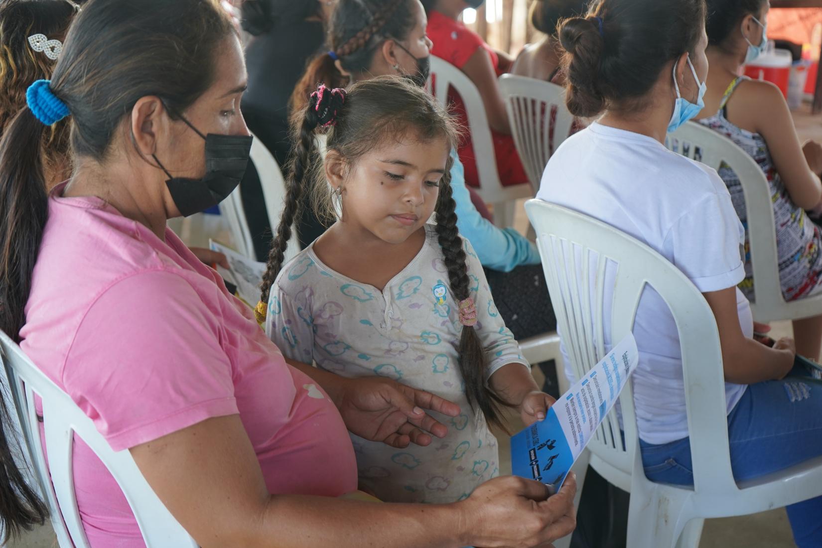 Una niña y su madre sentadas en una silla leen un folleto en una jornada de sensibilización.