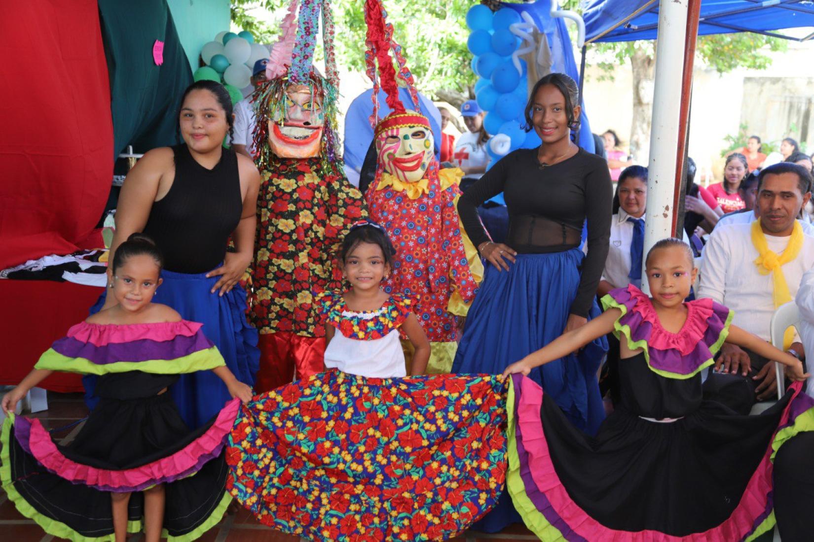 Un grupo de mujeres y niñas con vestidos tradicionales miran a cámara.