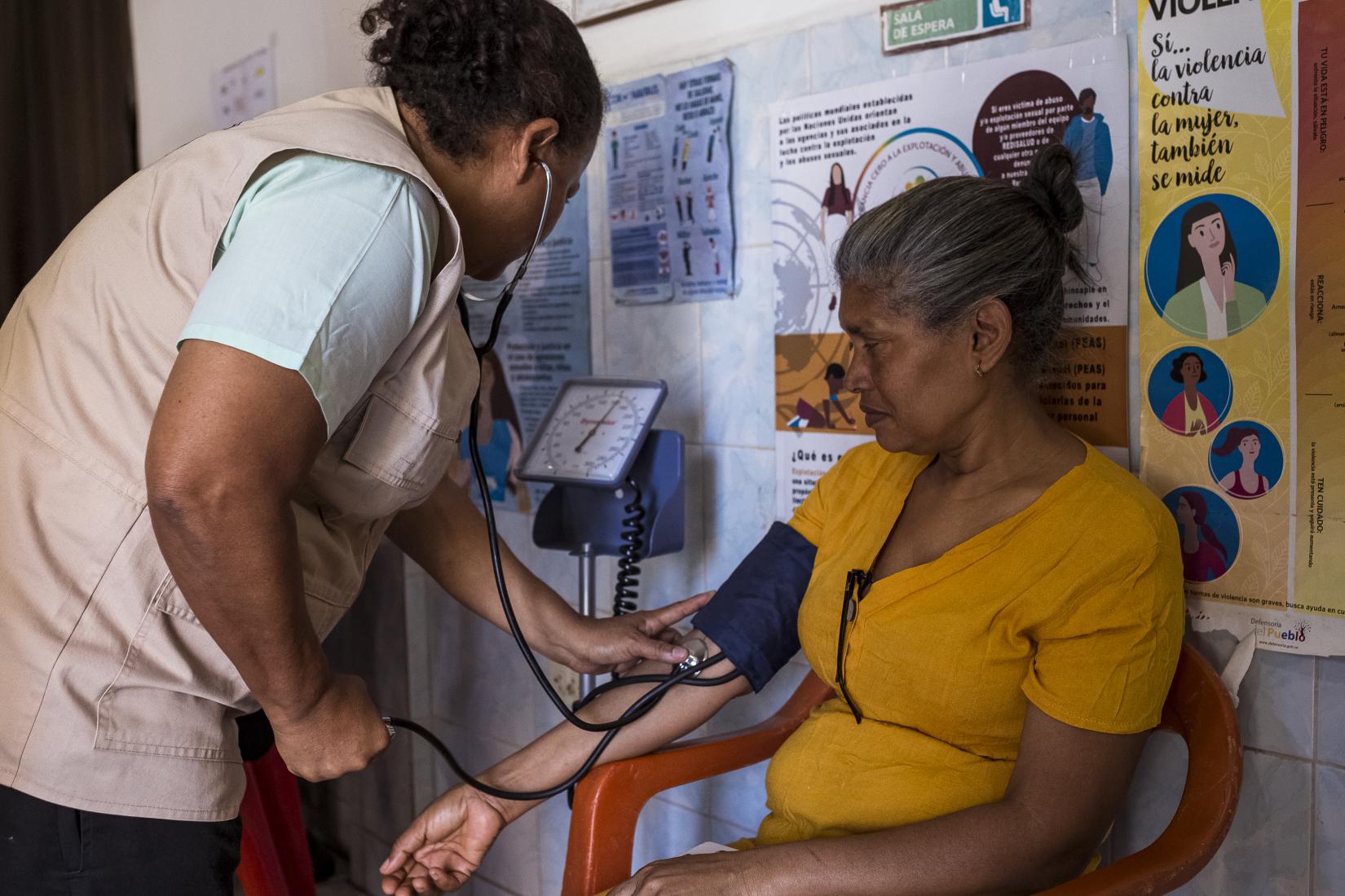 Una mujer personal de salud le toma la tensión a otra mujer en una jornada de salud.