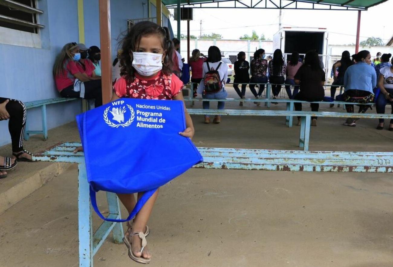 Thania, una niña de 4 años, sentada en una banca sostiene una bolsa del Programa Mundial de Alimentos (WFP)